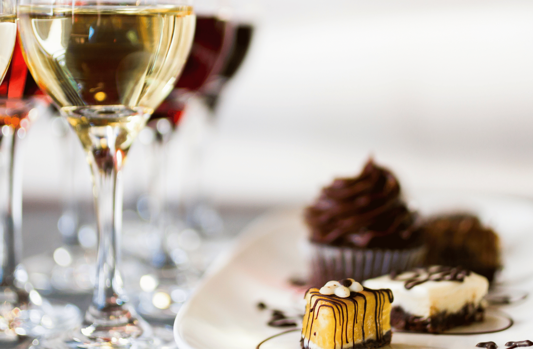 A glass of wine is sitting on a table next to a plate of desserts.