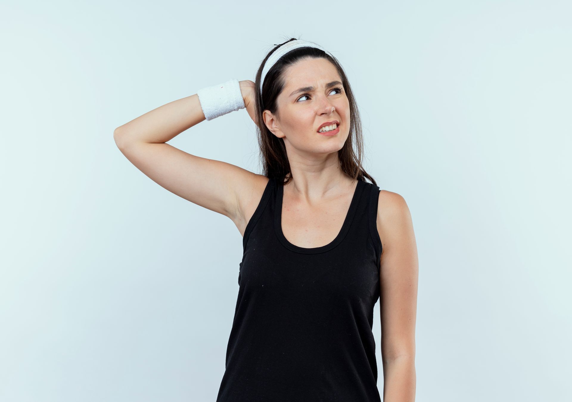 A woman wearing a black tank top and white wristband scratches her head with a confused expression against a light background.