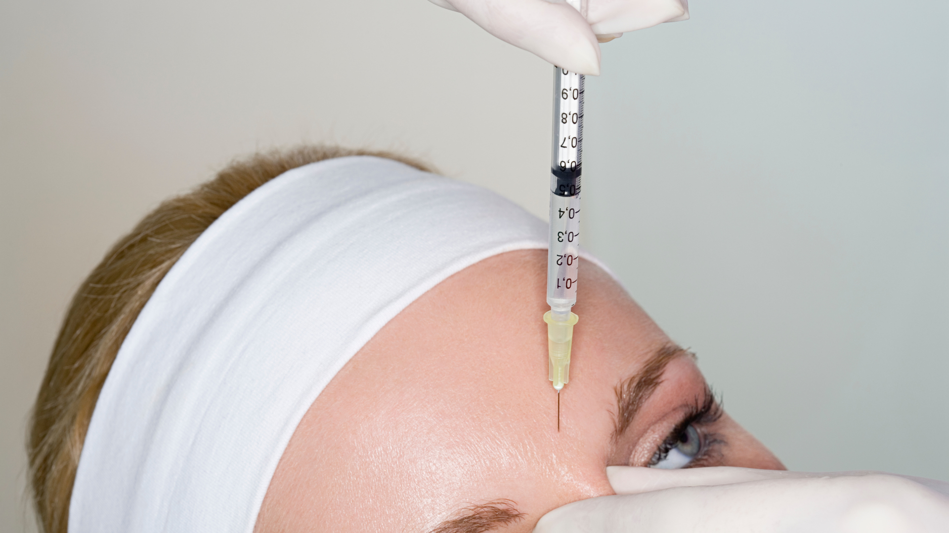 Woman in bed, holding phone, with hand on forehead, looking stressed.