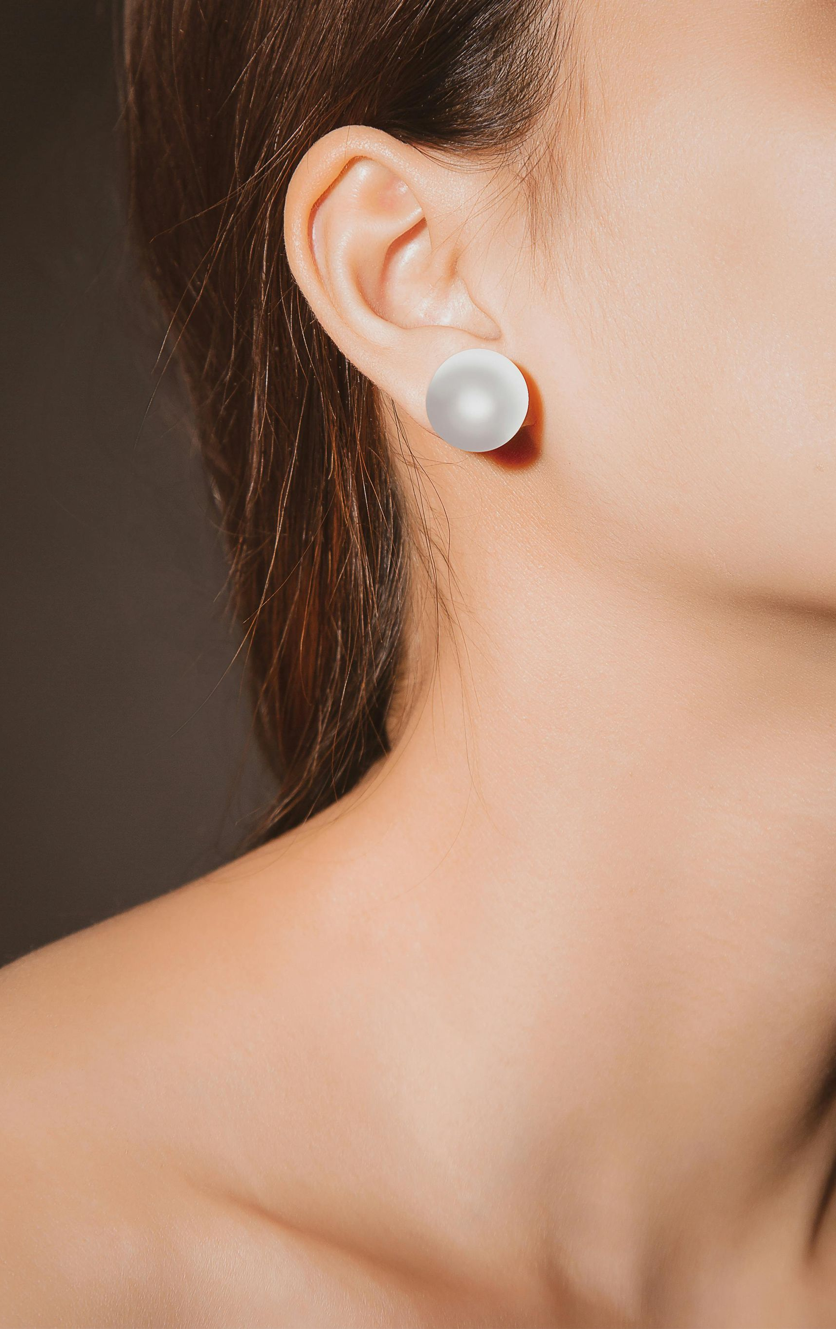 Woman with fair skin wearing a large, white pearl earring. Shoulder and ear visible.