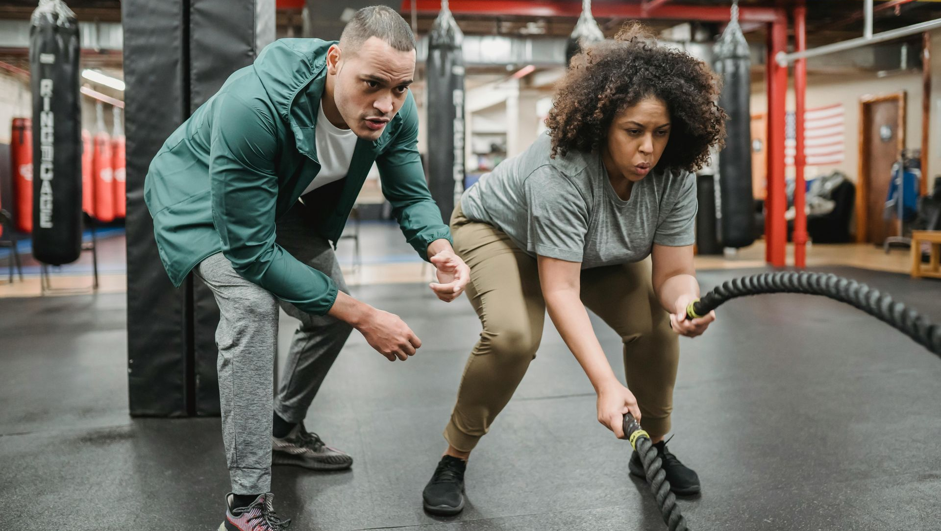 Man coaching woman on battle rope exercise in a gym.
