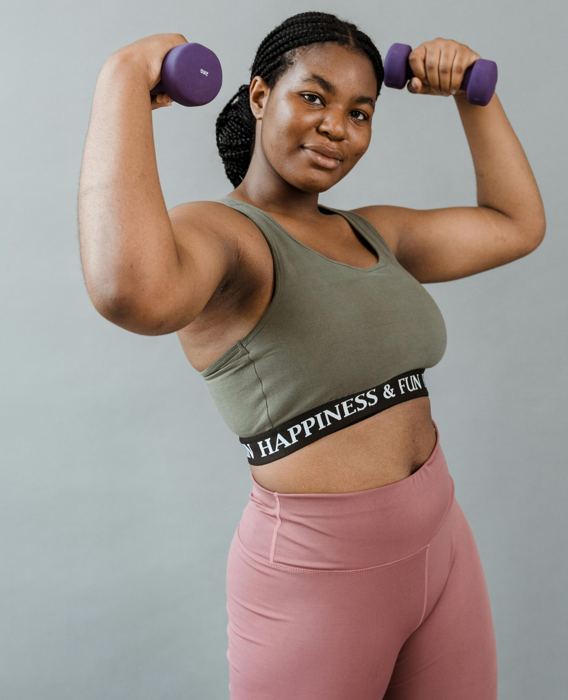 Woman in workout clothes lifts weights, smiling.