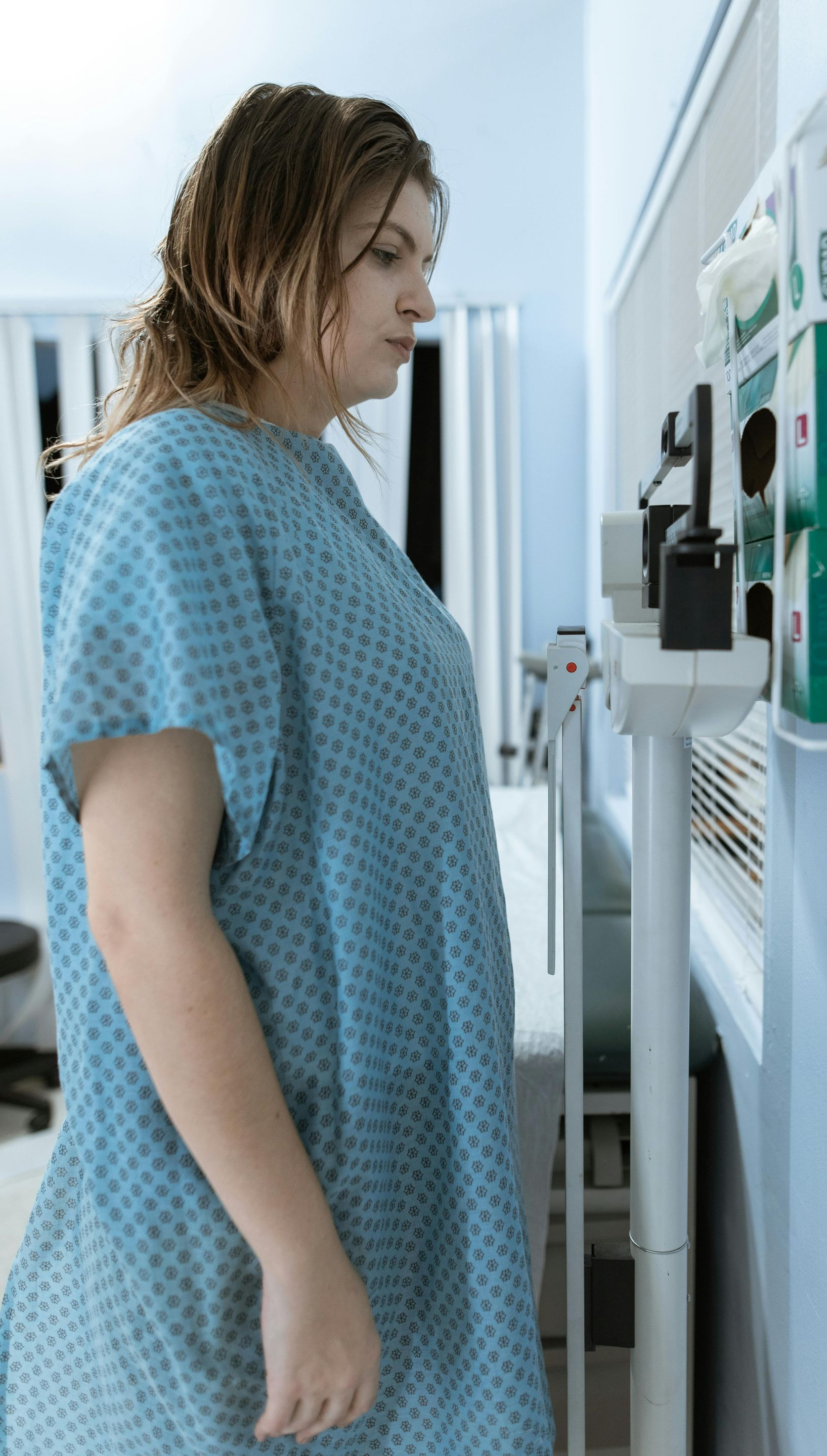Woman in hospital gown standing on a scale in a doctor's office.
