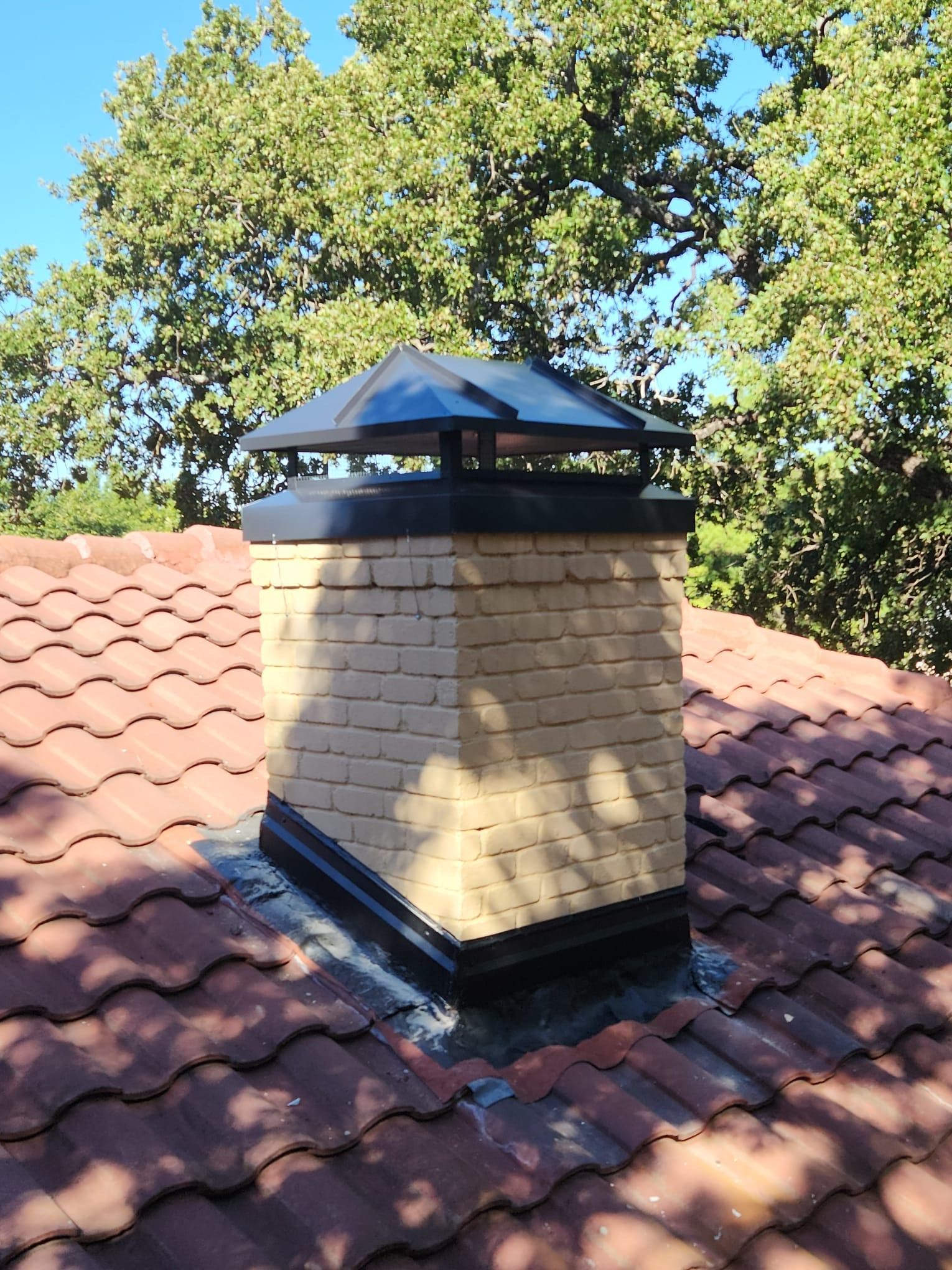 A brick chimney is sitting on top of a tiled roof.