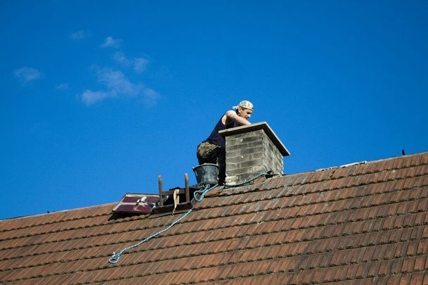 A man is sitting on top of a chimney on a roof.