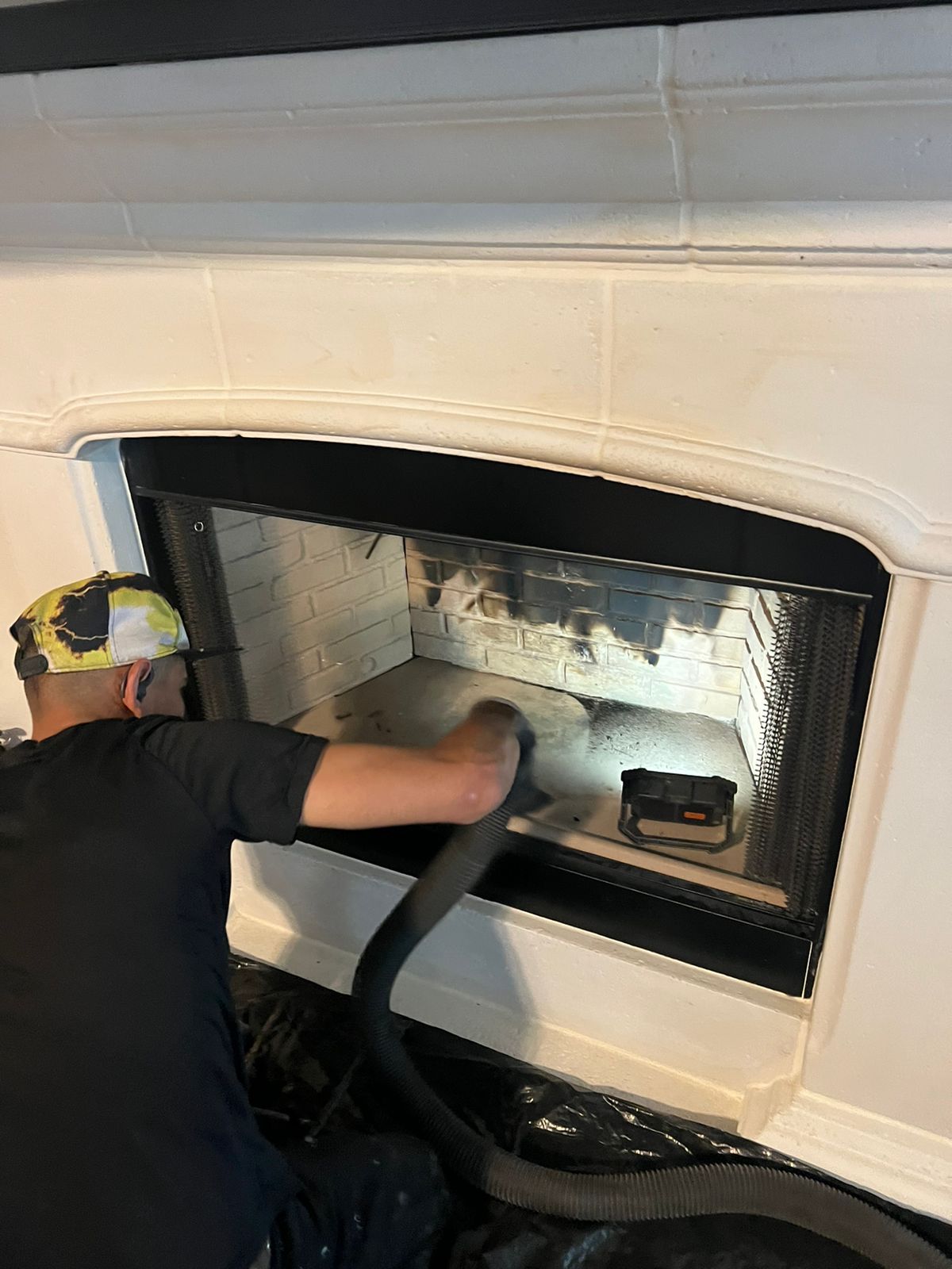 A man is cleaning a fireplace with a vacuum cleaner.