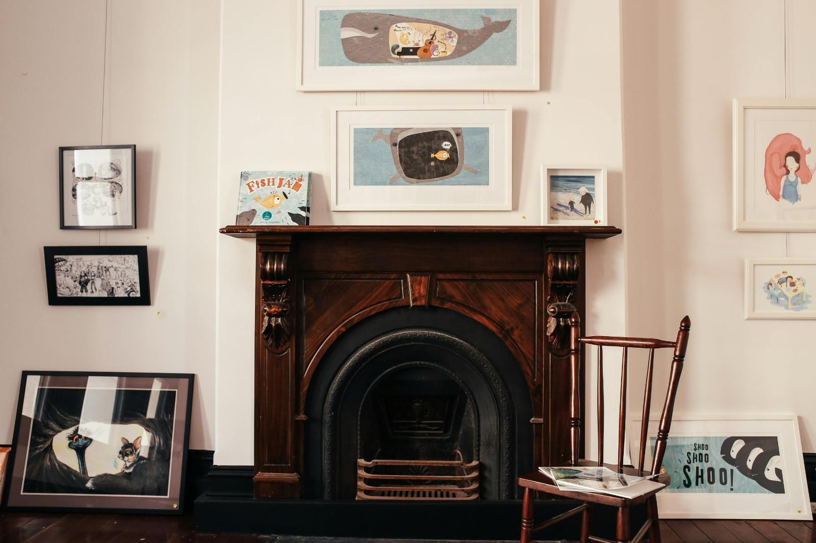 A living room with a fireplace , chair , and paintings on the wall.