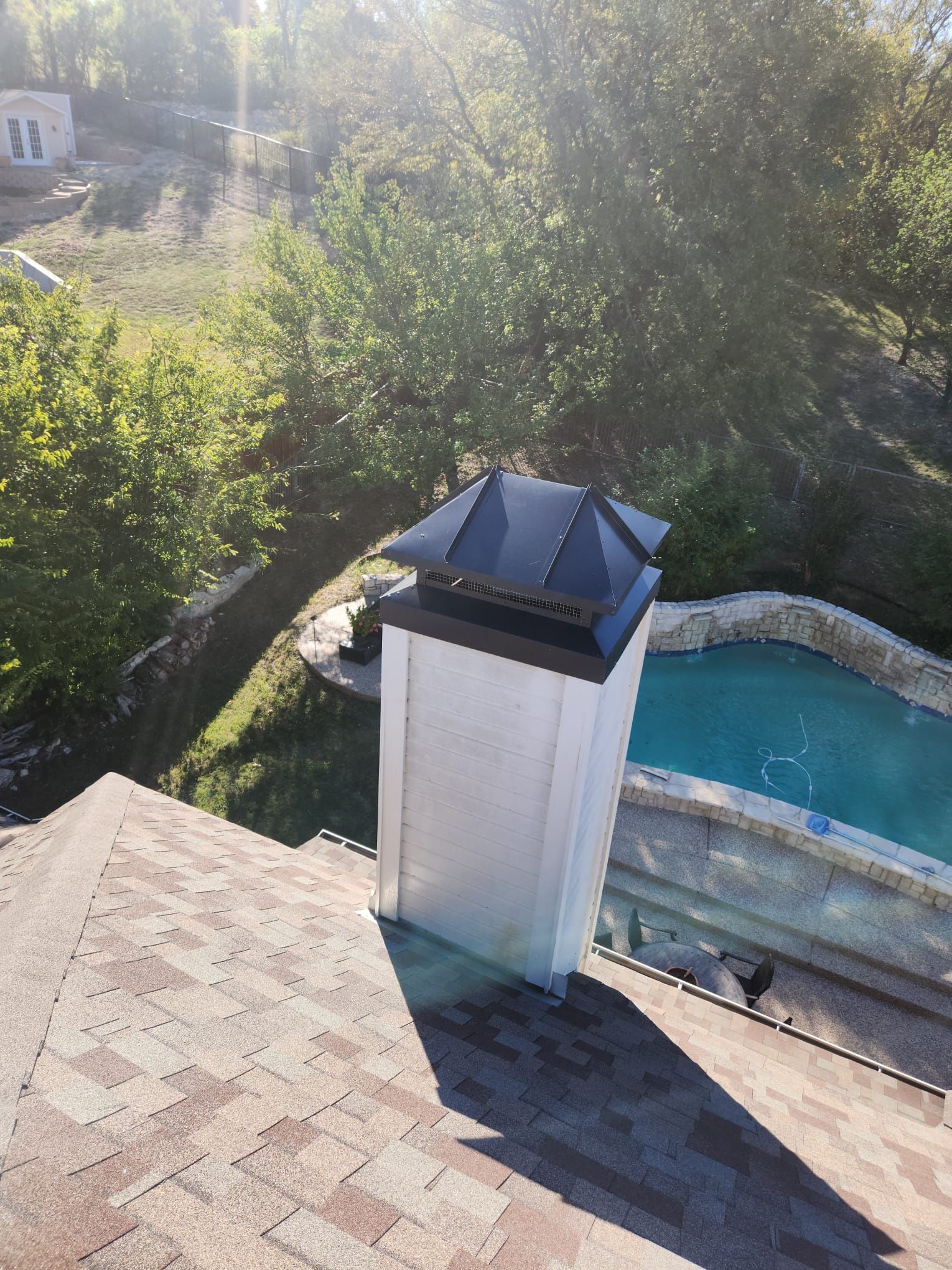 An aerial view of a roof with a chimney and a pool in the background.