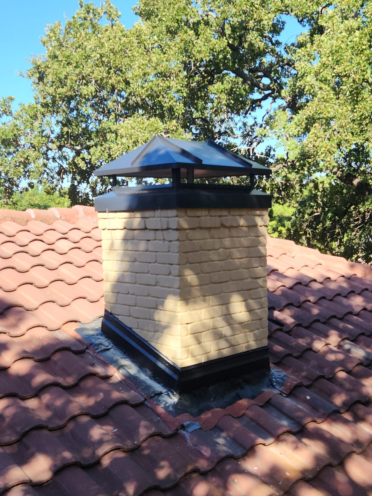 A chimney on top of a tiled roof with trees in the background