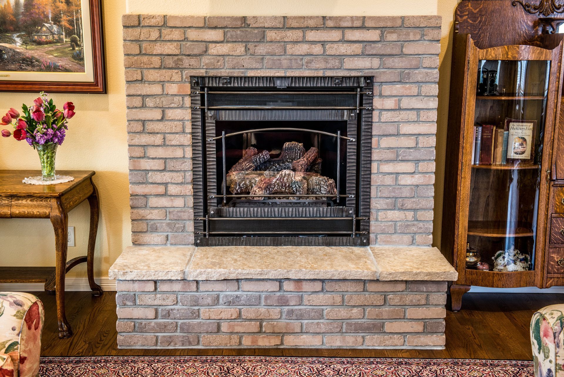 A living room with a brick fireplace and a vase of flowers.