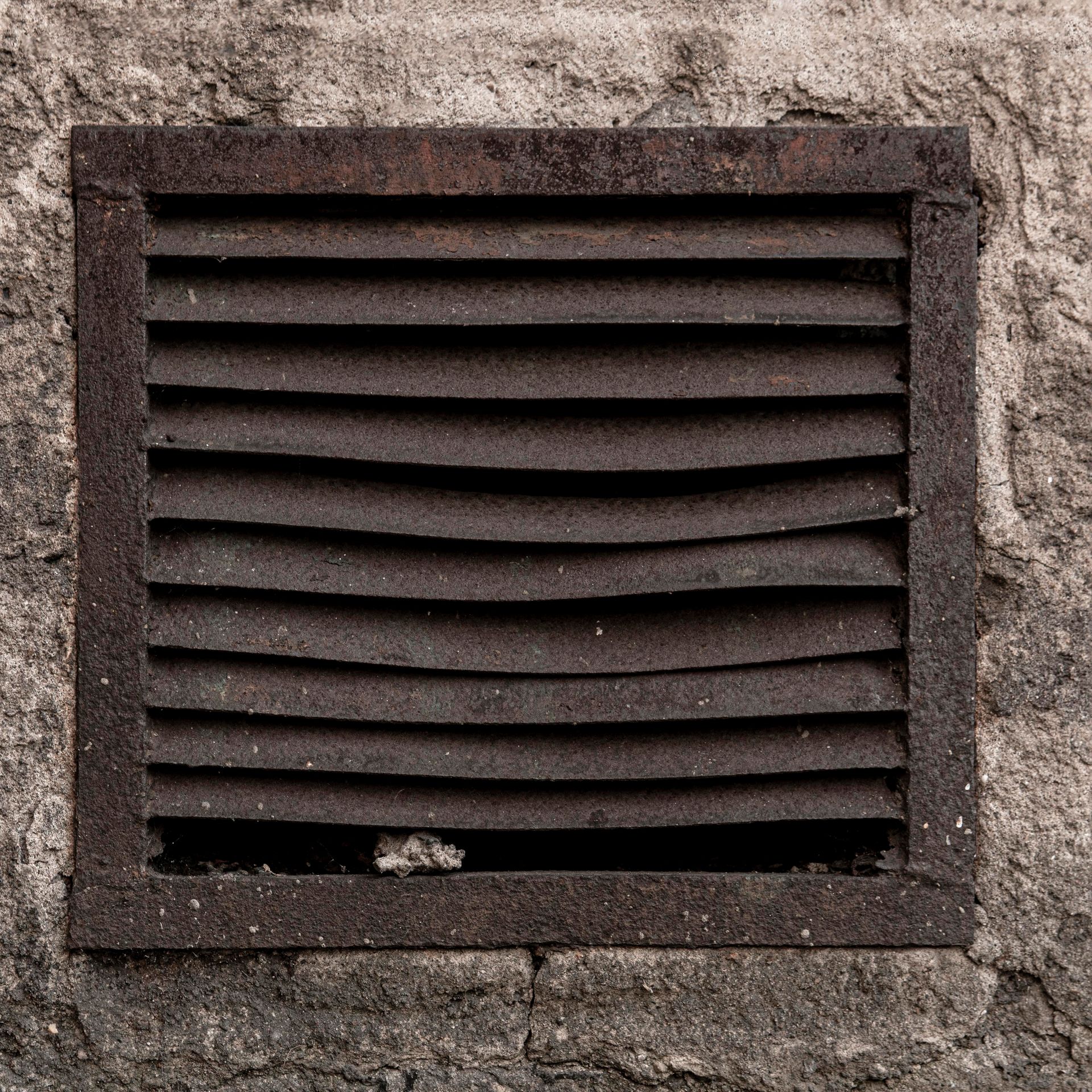 A rusty air vent is sitting on a concrete wall.