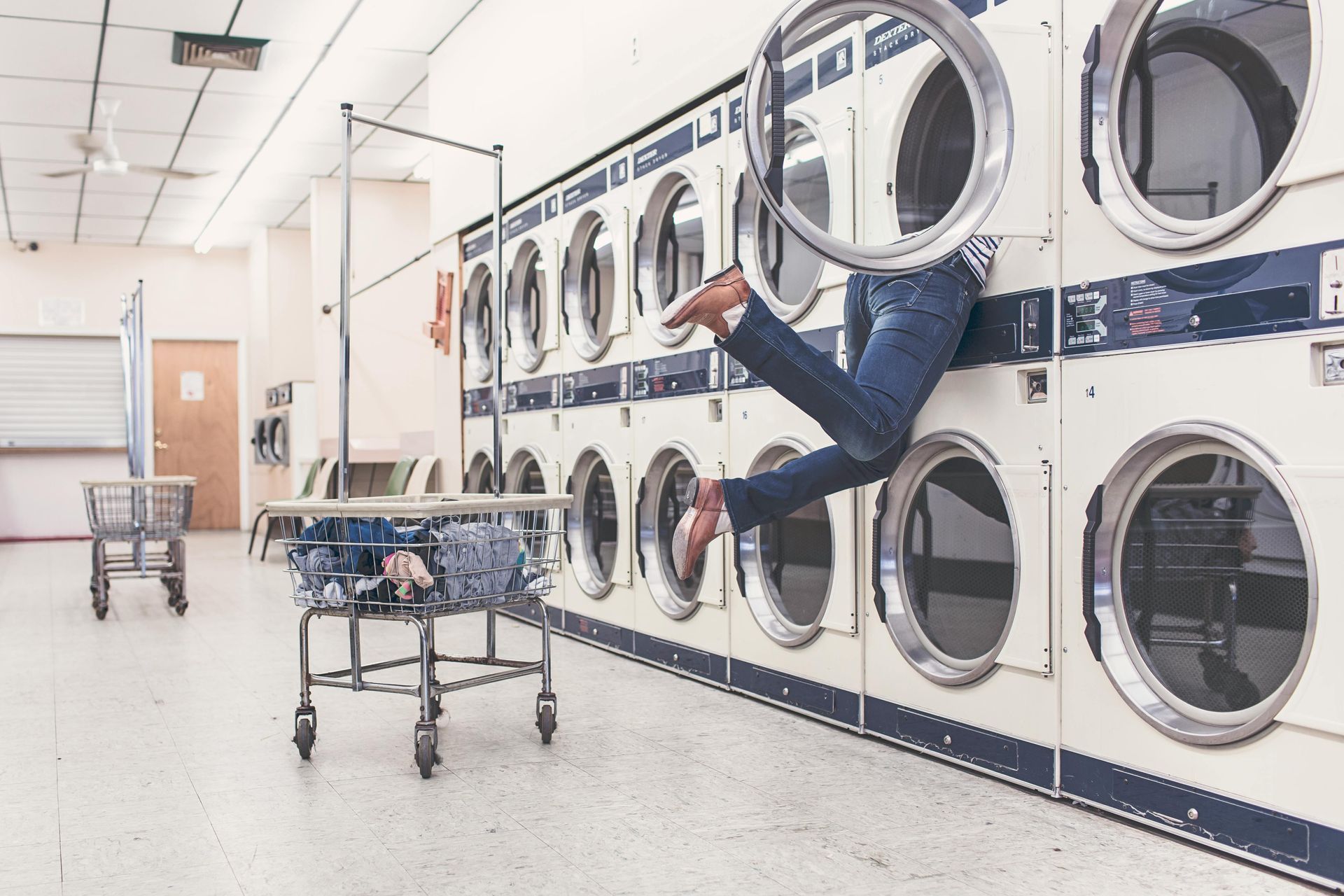 A person is jumping into a washing machine in a laundromat.