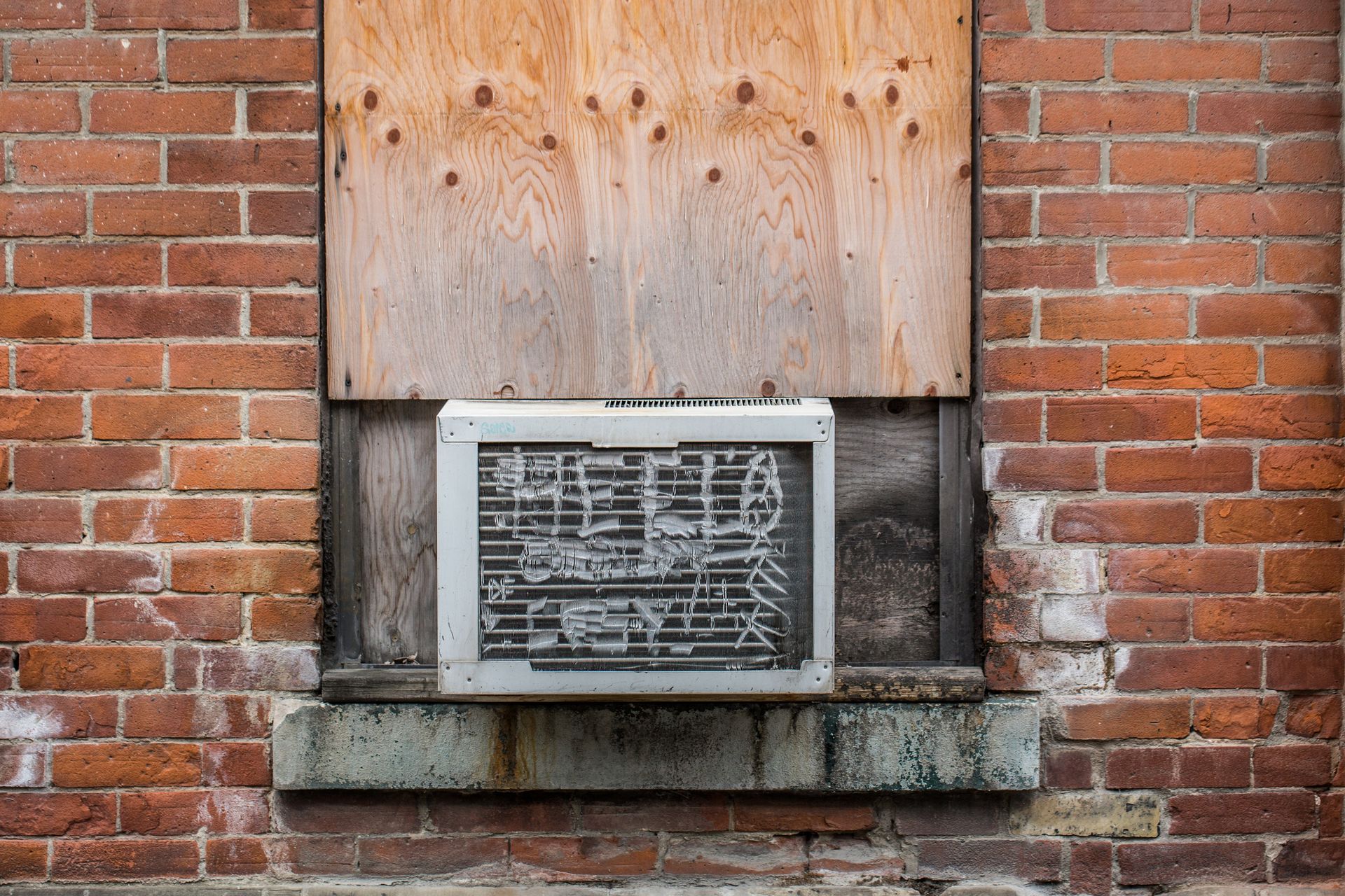 An air conditioner is sitting in a window on a brick wall.