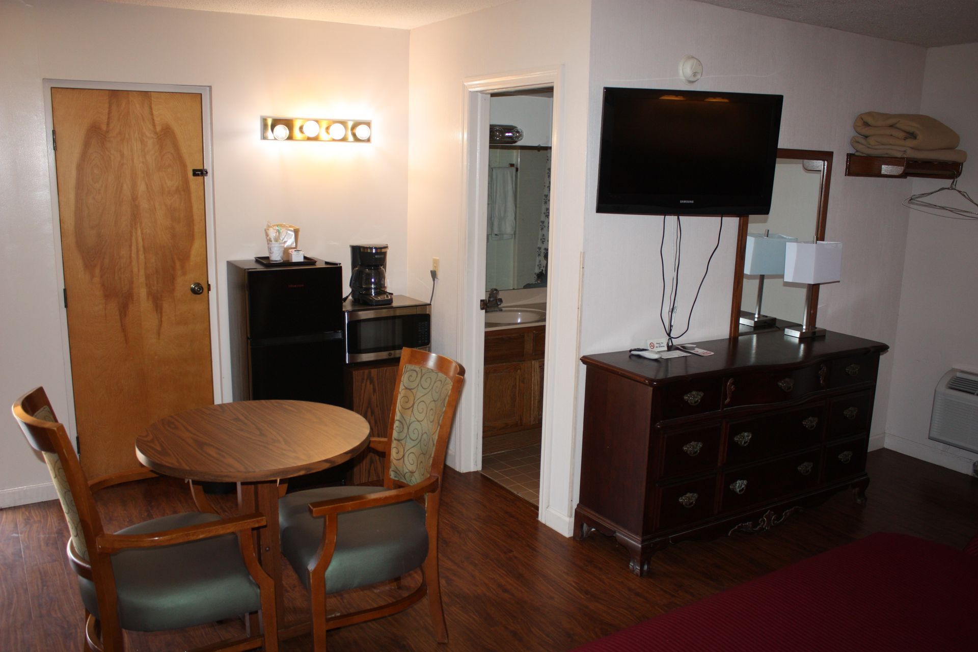 A hotel room with a table , chairs , dresser and television.