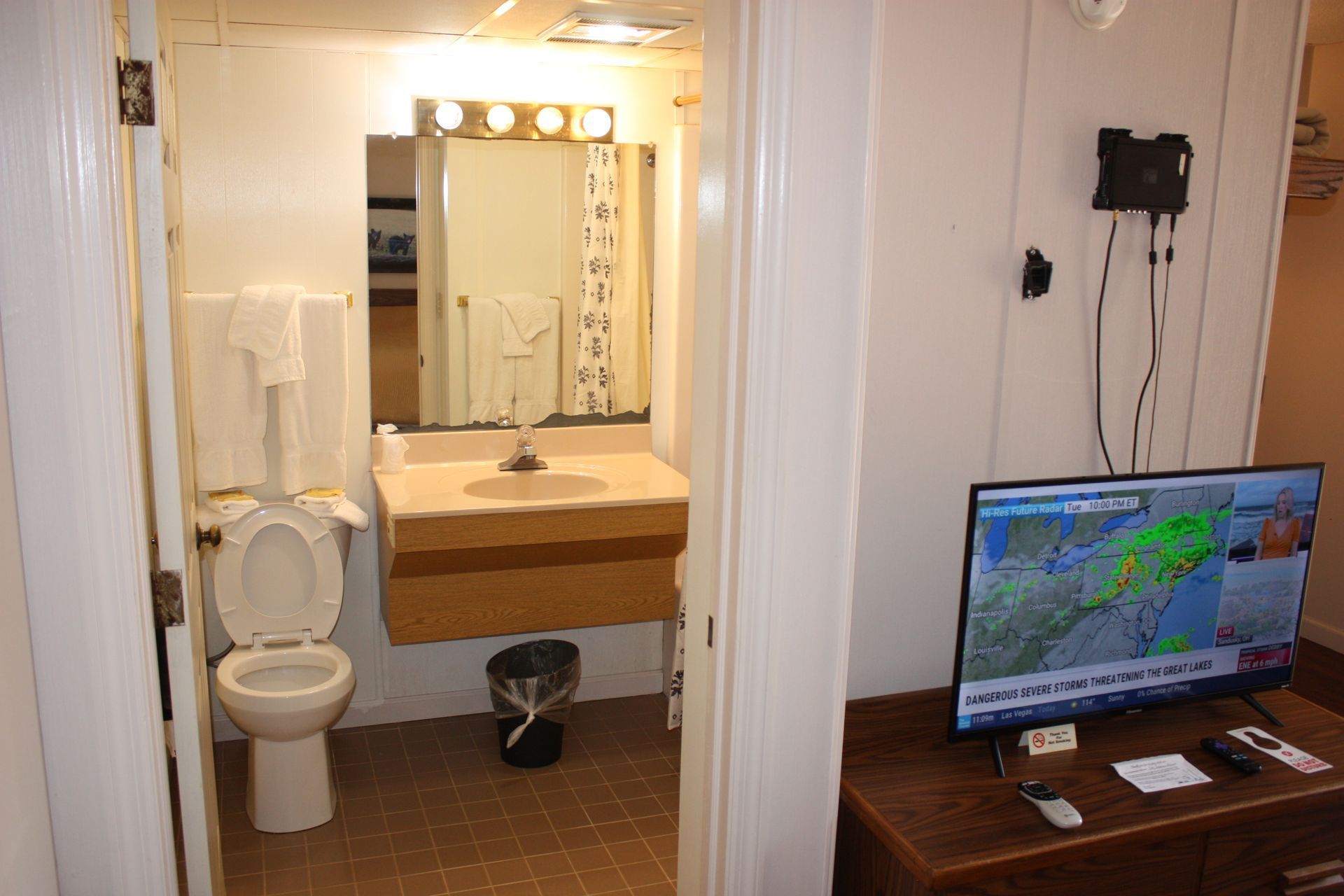 A bathroom with a toilet , sink and television.