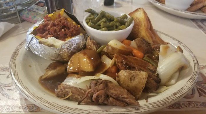 A plate of food with a baked potato and green beans on a table.