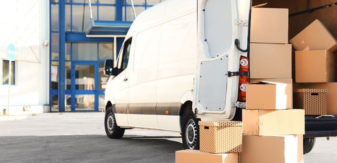 White delivery van with open back full of cardboard boxes, parked outside a building.
