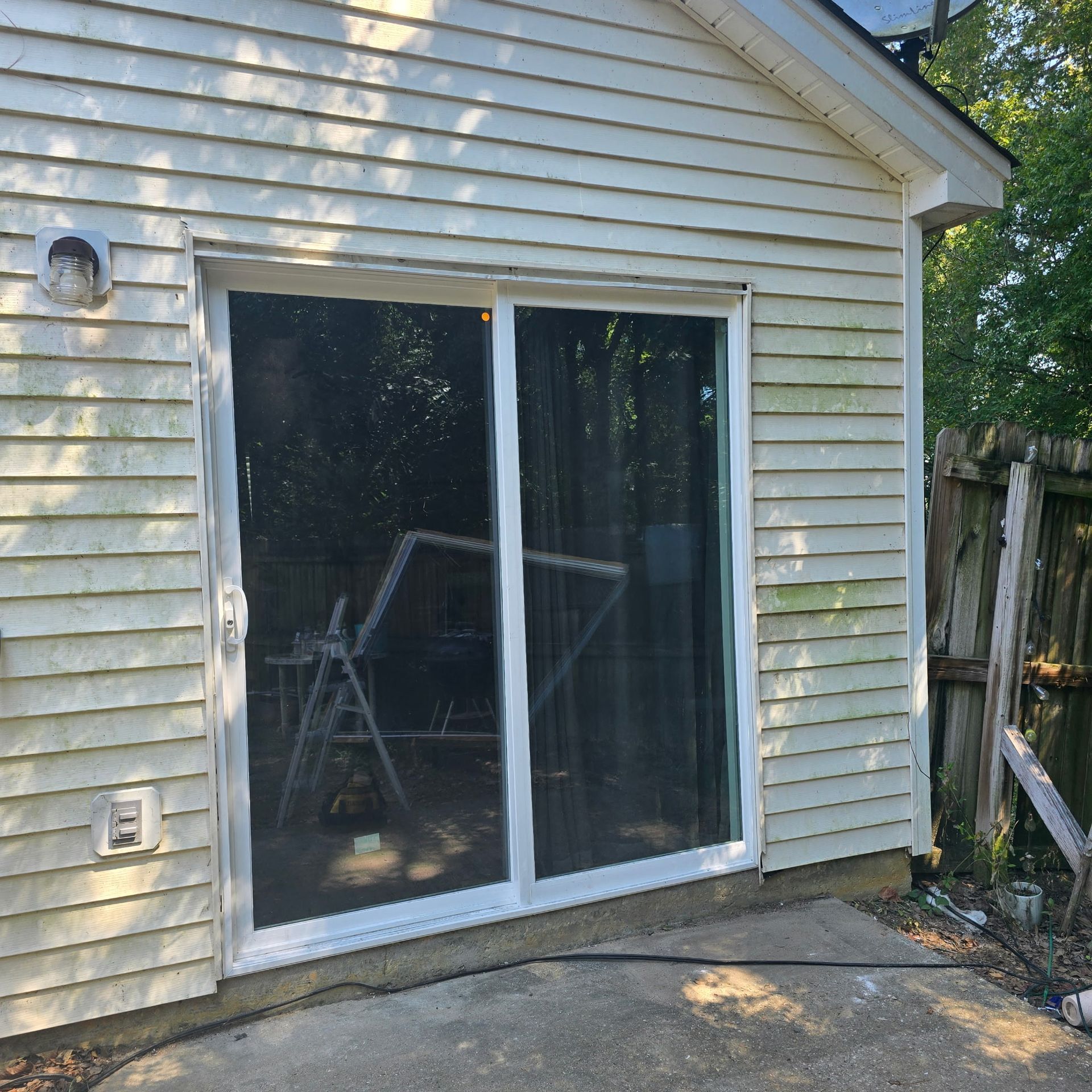Sliding glass door in a weathered white building, on a concrete patio.