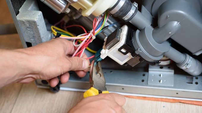 Person using pliers to cut a blue wire inside a dishwasher during repair.