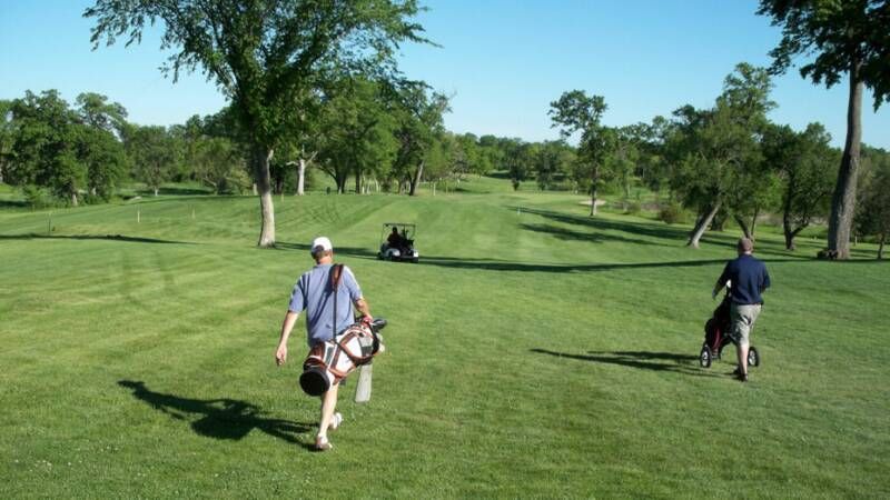 Two men are walking on a golf course carrying golf bags