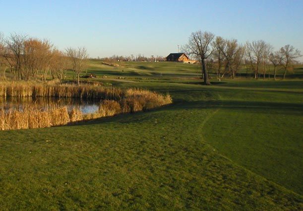 A golf course with a pond and a barn in the background