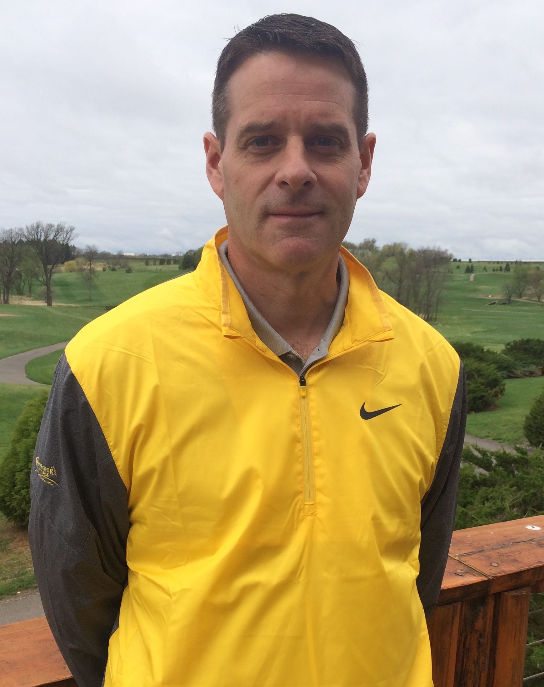 A man wearing a yellow nike jacket stands in front of a golf course