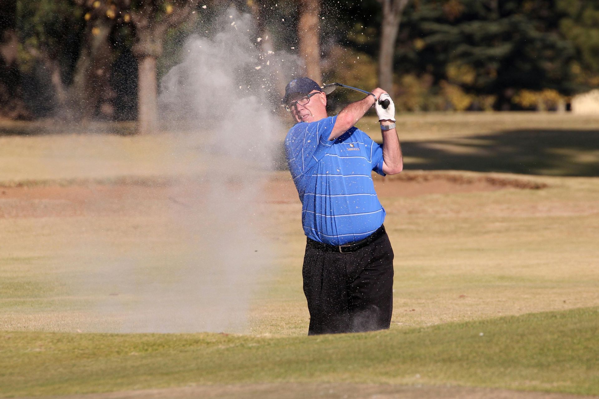 A man is hitting a golf ball out of a bunker on a golf course.