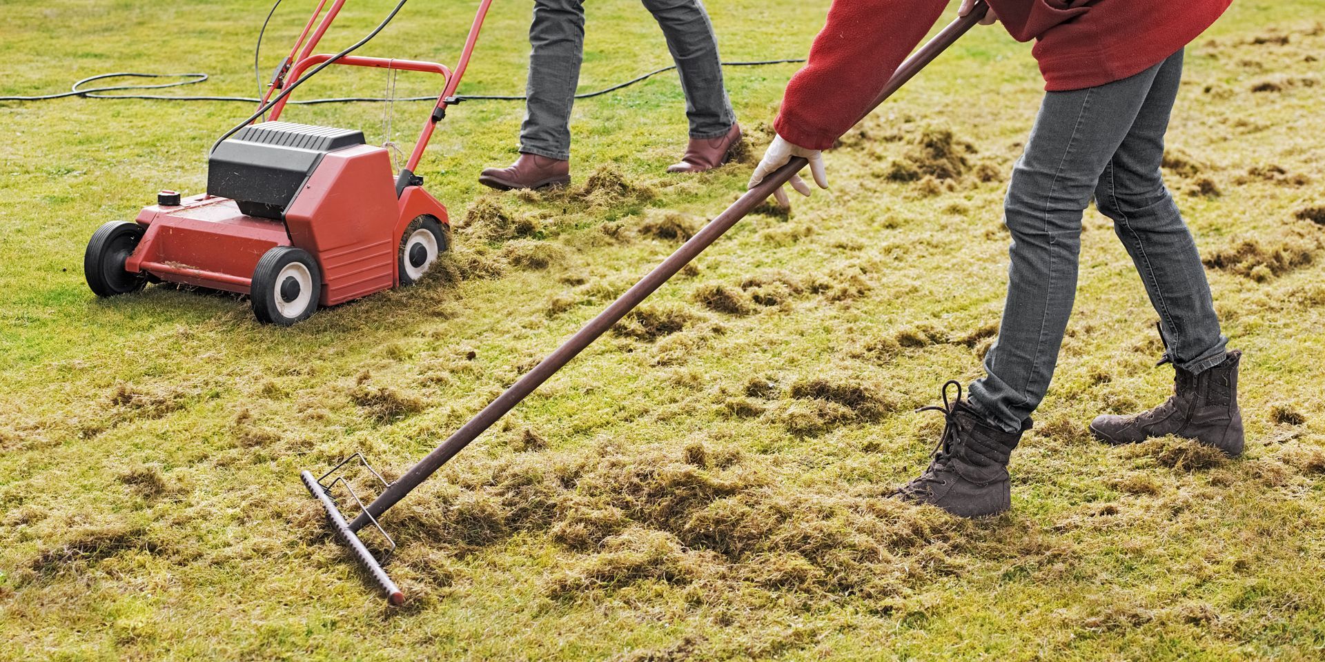 A person is raking the grass next to a lawn mower.