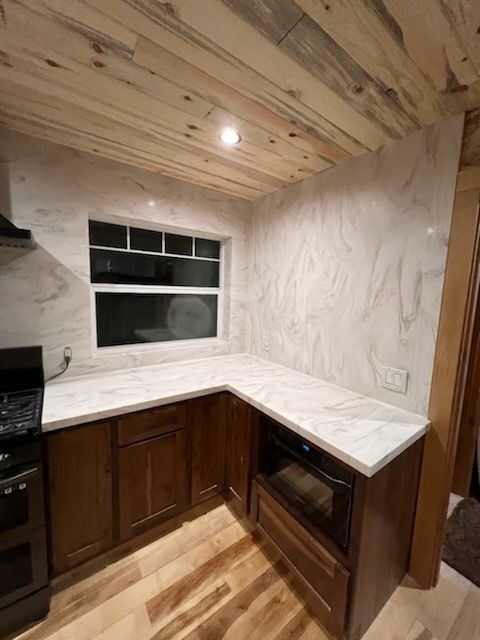 A kitchen with marble counter tops , wooden cabinets , a stove and a window.