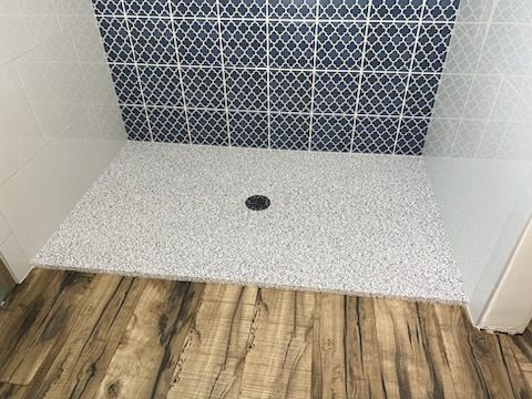 A shower stall with a wooden floor and blue tiles on the wall.
