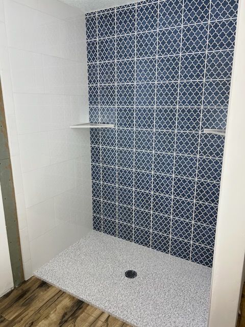 A shower with blue tiles on the wall and a white floor.