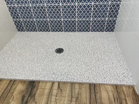 A shower stall with a wooden floor and blue tiles on the wall.