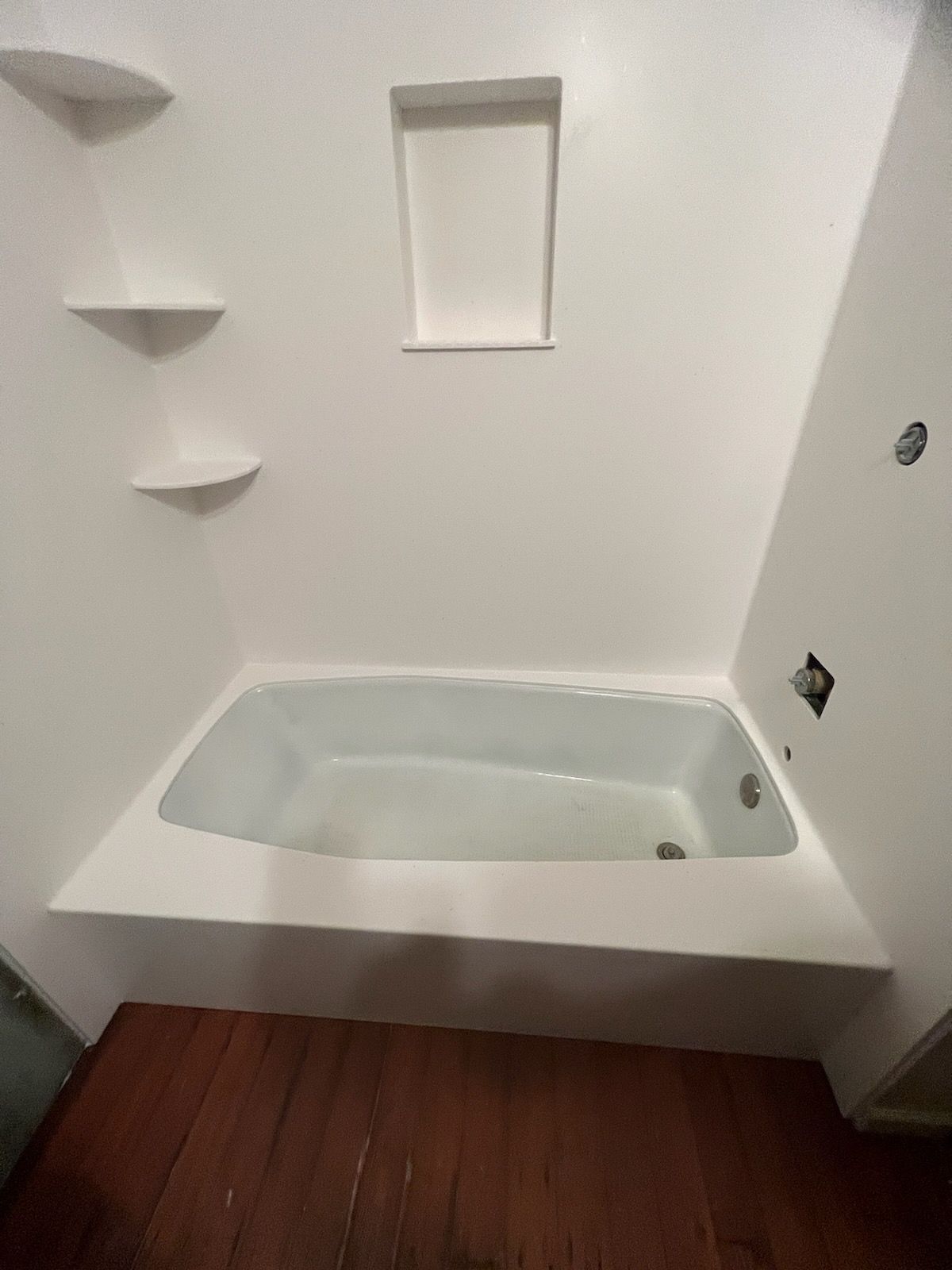 A bathtub in a bathroom with white walls and shelves