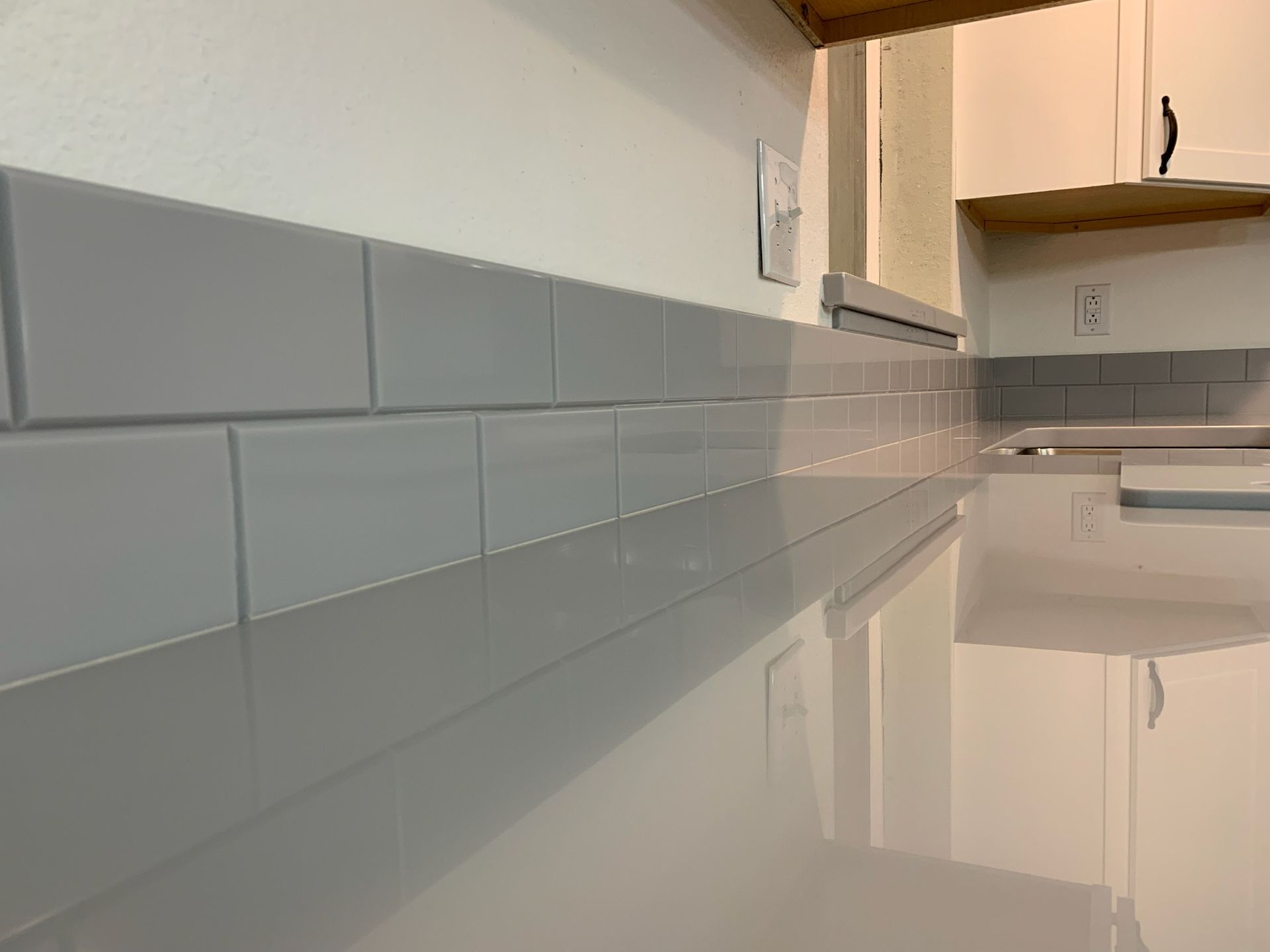 A kitchen with white cabinets and gray tiles on the wall.