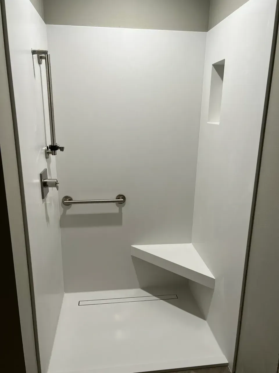 A white shower with a seat and a hand rail.