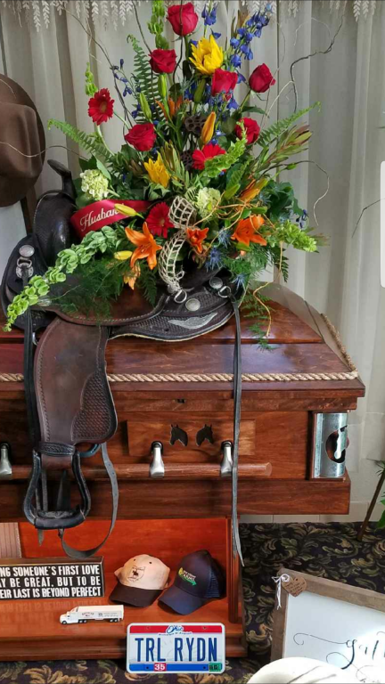a saddle sits on top of a coffin with flowers and a license plate that says trl rydn