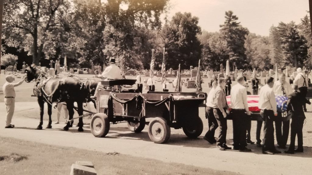 a black and white photo of a horse drawn carriage in a cemetery