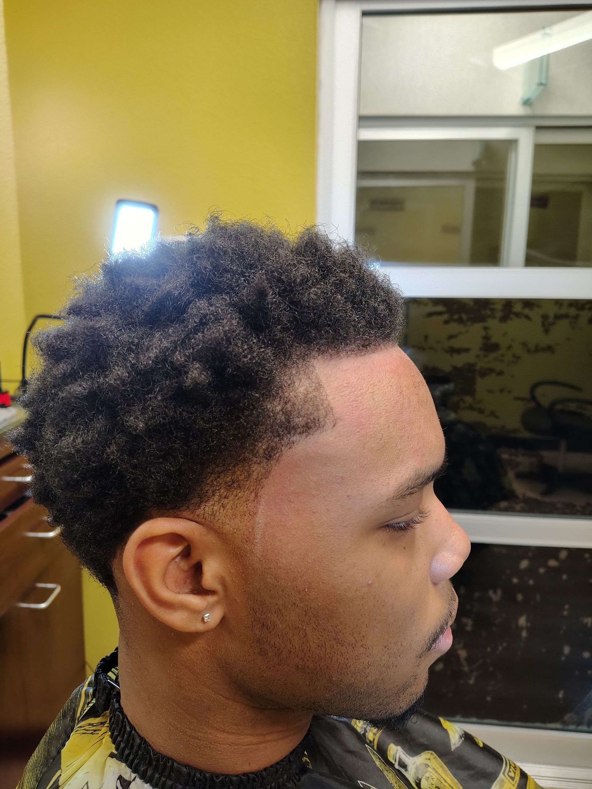 A person with a textured, faded haircut and a clean-lined hairline, sitting in a barbershop chair.
