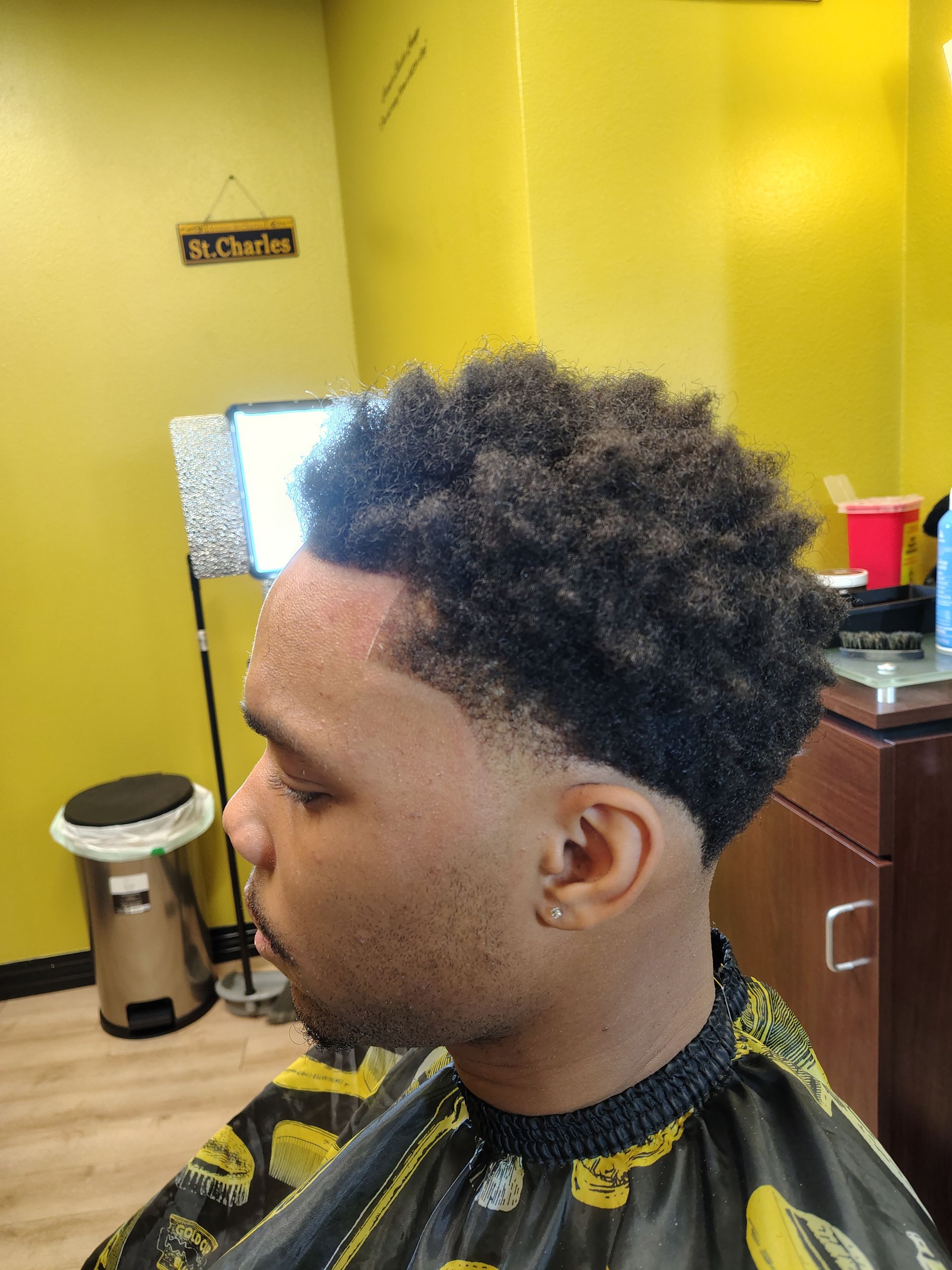 A person with a short, textured haircut with a faded neckline, seated in a salon chair against a yellow wall.