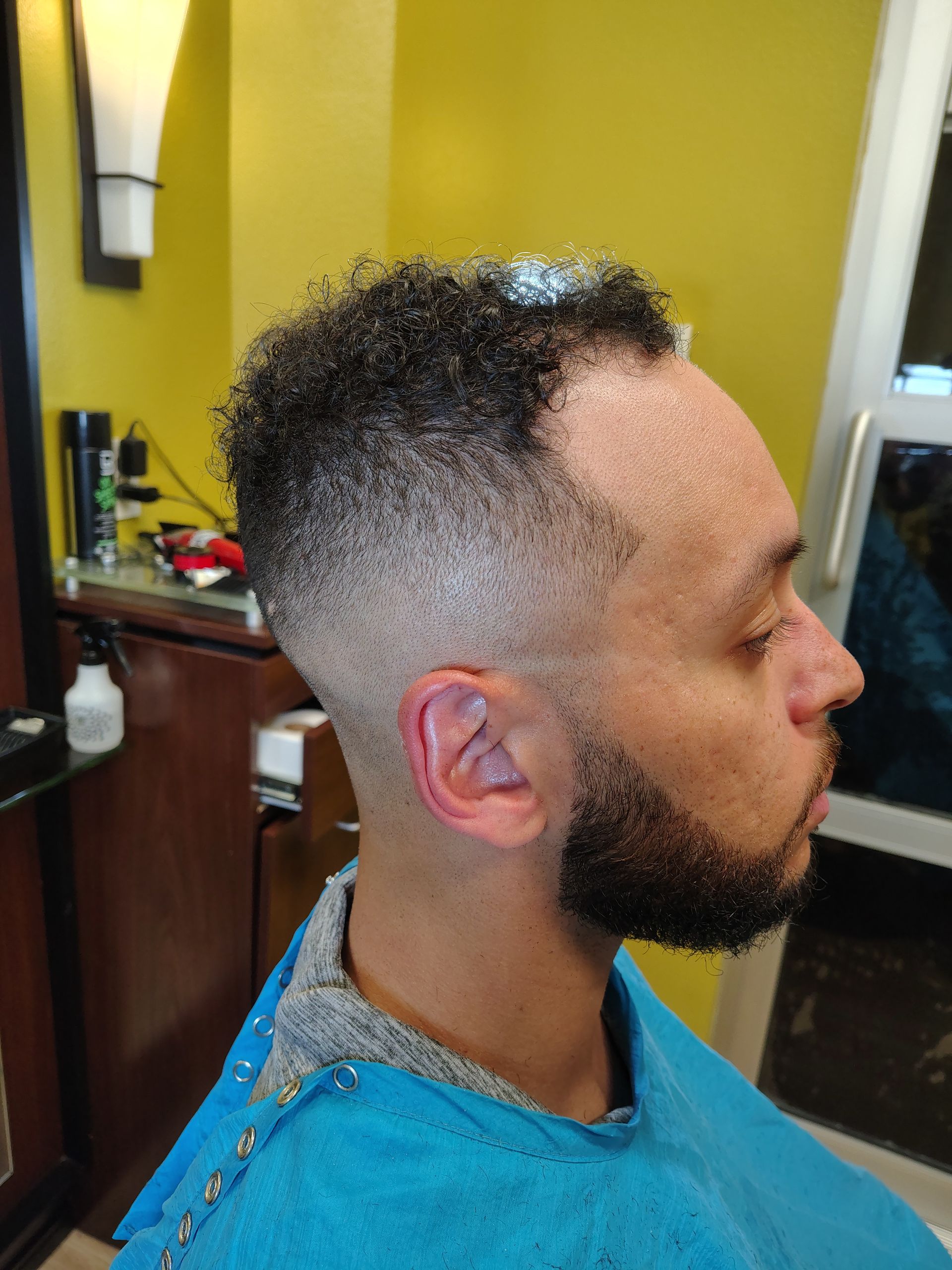 A person in a blue salon cape with a fresh skin fade haircut, seen in profile while in a barbershop.