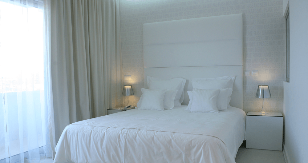 Um quarto com uma cama, mesas de cabeceira, cortinas e lâmpadas.