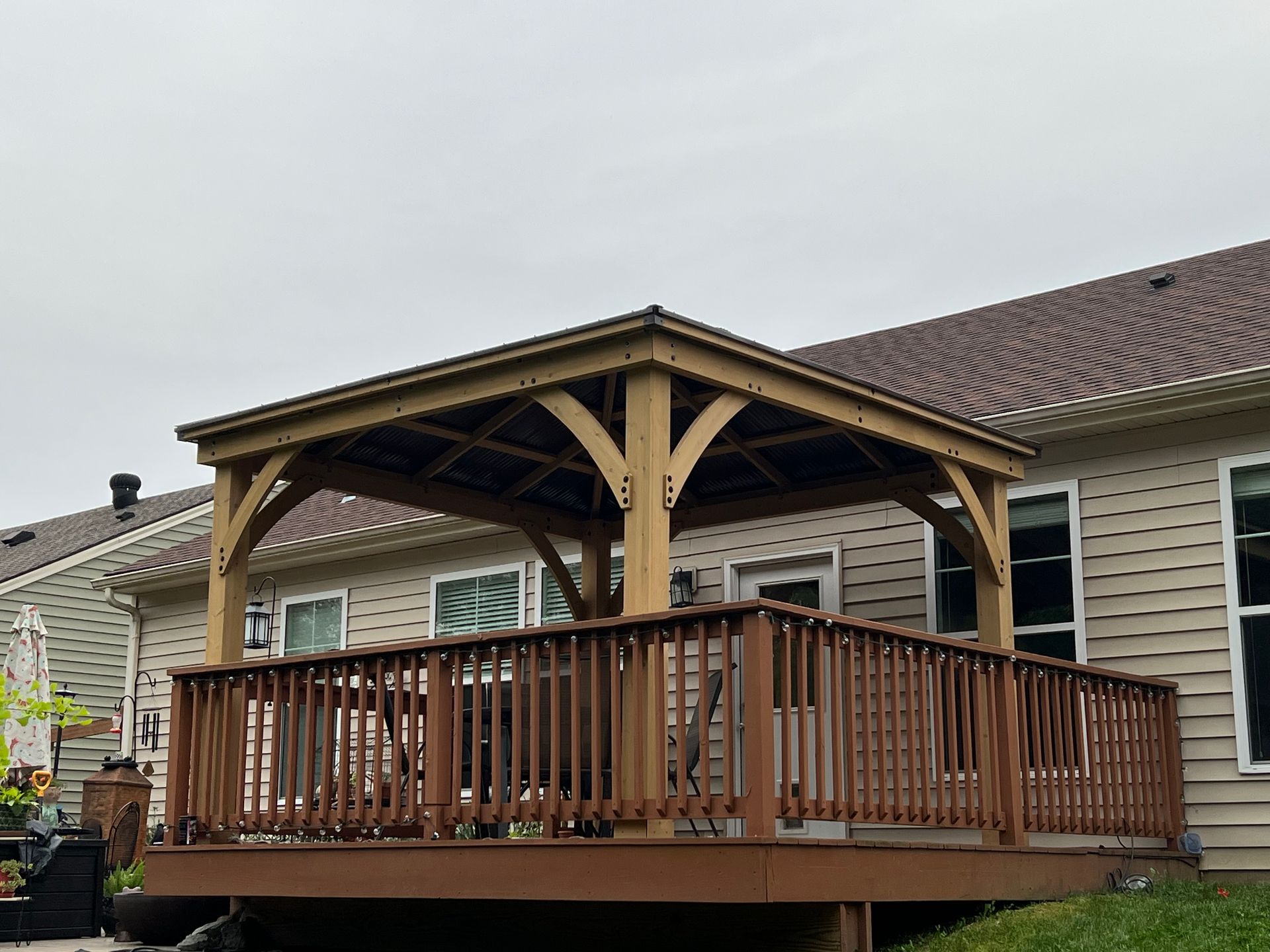 A wooden deck with a gazebo on top of it in front of a house.