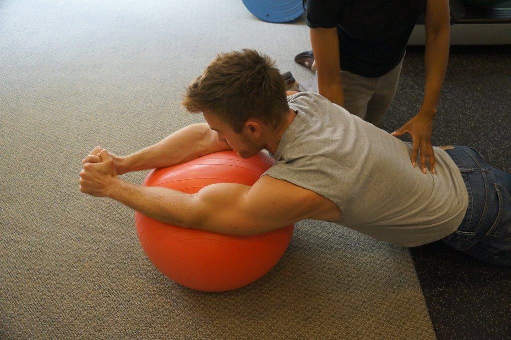 A man is doing a plank on an orange exercise ball.