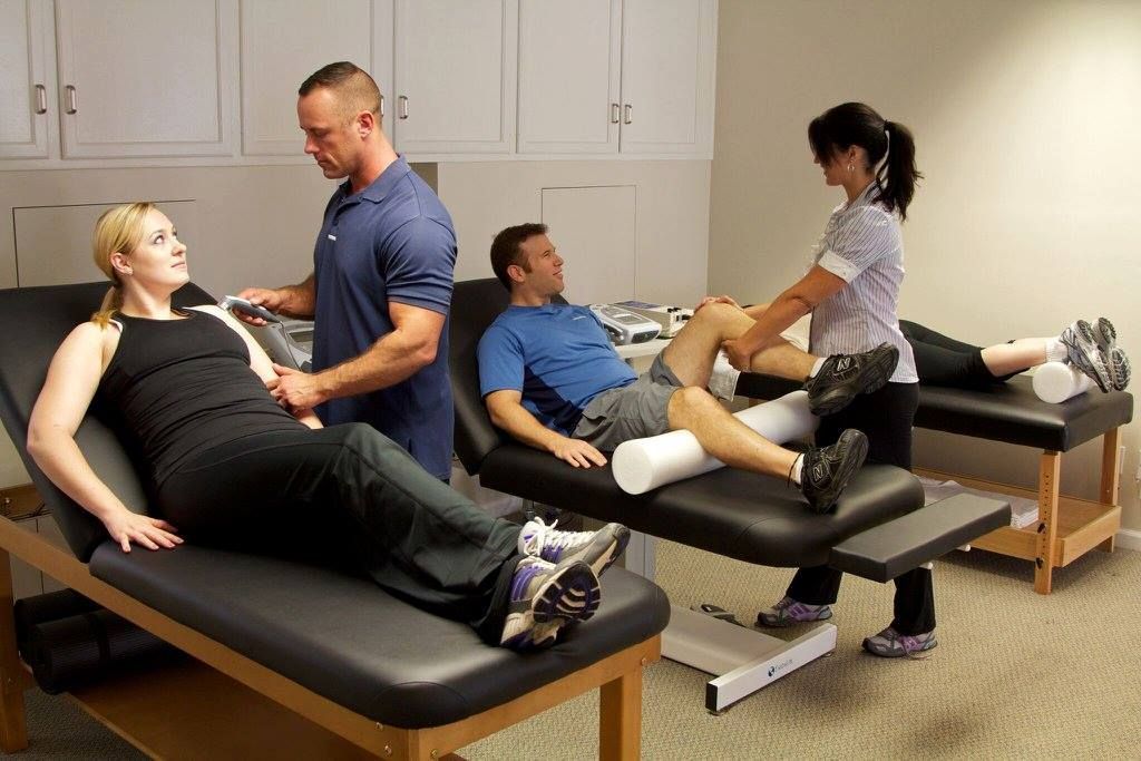 A woman is laying on a table while a man and a woman work on her leg