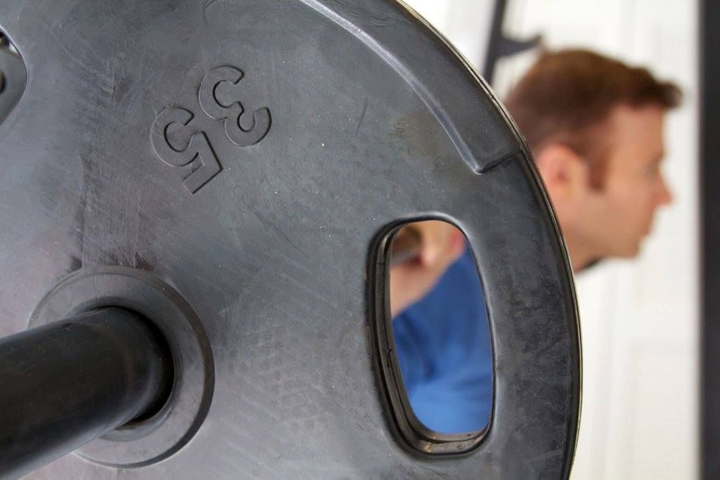 A close up of a barbell with a man in the background.