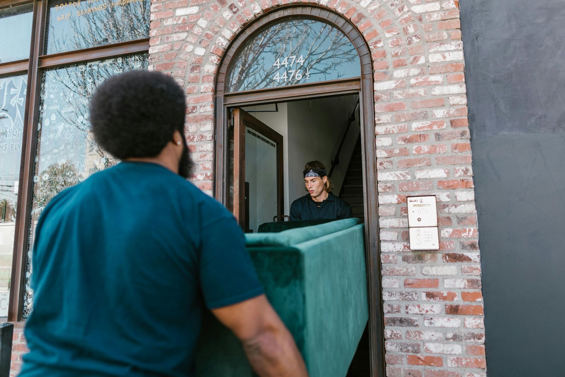 Two people carrying a teal couch through a brick doorway.