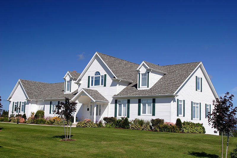 White house with gray roof and green shutters on a sunny day.