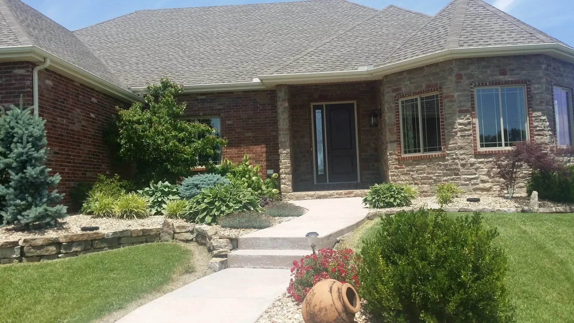 A brick and stone house with a curved path leading to the front door, surrounded by landscaping.