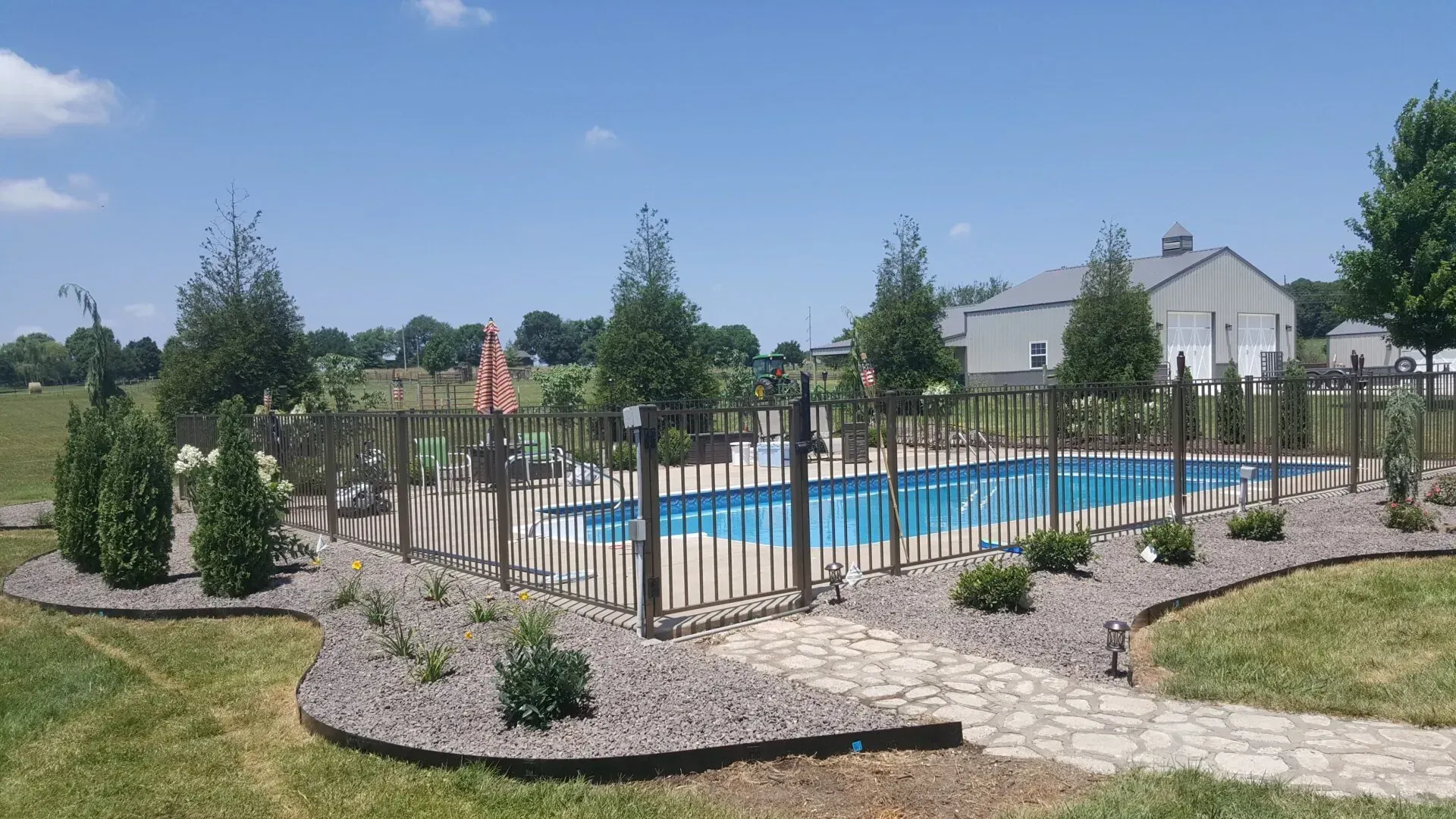 Green field of mown grass under a blue sky with fluffy white clouds; trees and a building are in the distance.