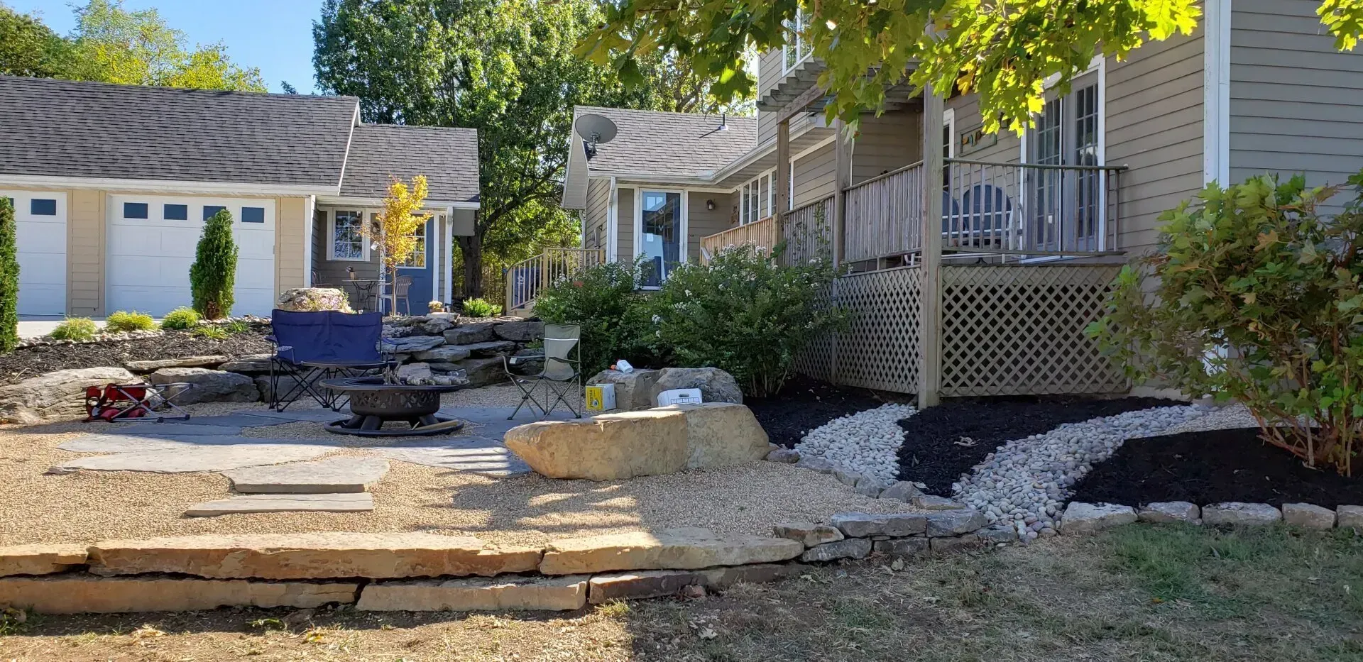 Asphalt driveway next to freshly mowed green lawn with striped mowing pattern, trees in the background.
